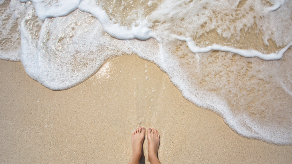 feet on sand standing by the ocean