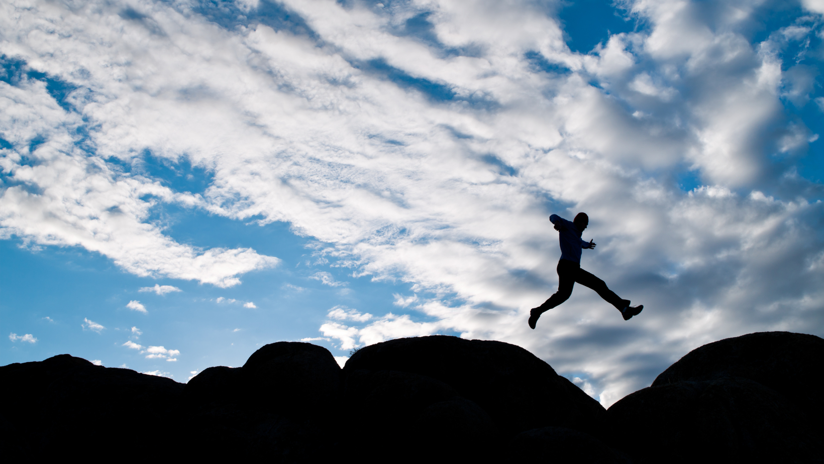 Silhouette of a person jumping across hilltops
